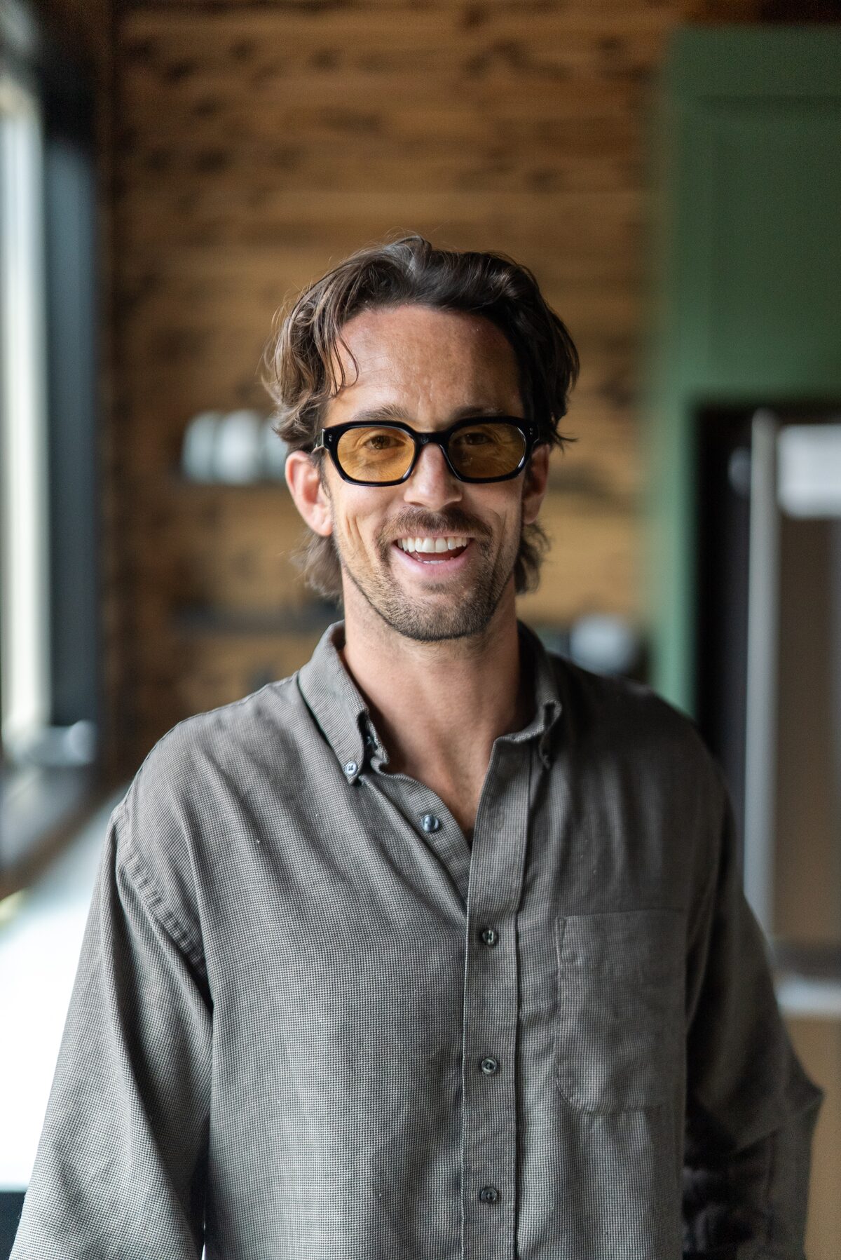 Evan J. Montgomery, smiling, in a gray shirt and amber glasses